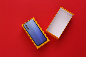 New modern smartphone in packing box on red background. Top view. Minimalism.