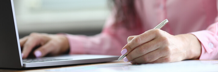 Woman makes notes with pen on sheet and on laptop. Atmosphere activity is very conducive to fruitful work. Good specialist manages to carry out main work. High workload at work