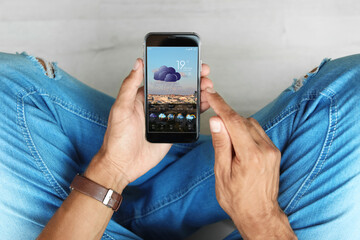 Man using weather forecast app on smartphone indoors, closeup