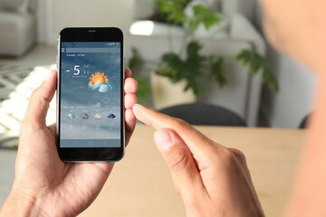 Wall Mural - man using weather forecast app on smartphone indoors, closeup