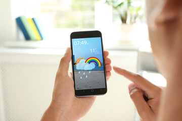 Wall Mural - man using weather forecast app on smartphone indoors, closeup