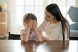 © fizkes - Caring mother calming and hugging crying upset little daughter, sitting at desk together, loving mum expressing support, comforting offended preschool girl, children psychologist concept