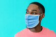 © Carlos David - Portrait of a young african man wearing mask for coronavirus looking to side, against blue studio background