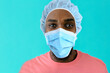 © Carlos David - Portrait of a young african person wearing mask and hair cap for coronavirus protection looking at camera, against blue studio background