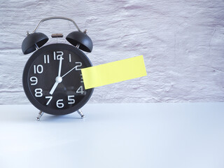 The black clock with yellow post-it note on white background, Copy space for your text. .