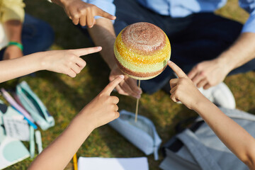Wall Mural - top view close up of group of children pointing at model planet while enjoying outdoor astronomy cla