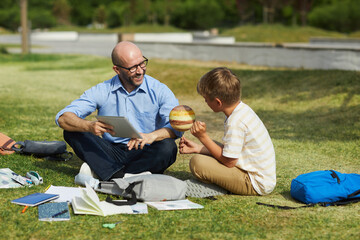 Wall Mural - full length portrait of smiling bald teacher talking to teenage boy holding model planet while enjoy