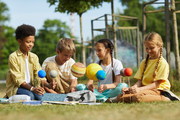Wall Mural - full length portrait of multi-ethnic group o children sitting on green grass and holding model plane