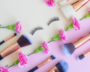 premium makeup brushes and  false eyelashes on a colored pink and yellow background, creative cosmetics flat lay