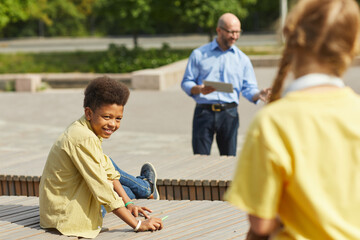 Wall Mural - portrait of smiling african-american boy looking over at classmate while enjoying outdoor lesson in 