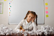 Shot of a small bored sleepy schoolgirl sitting near the table with many crumbled papers around