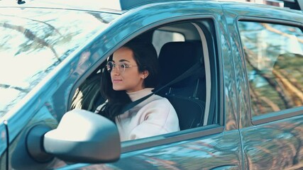 Wall Mural - Young woman sit in car during travelling break. Girl in forest sitting inside and unbuckle the seat belt an open car's door to go outside. Happy positive girl on video.