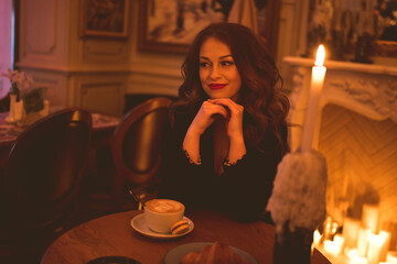 Smiling woman sittin in cafe with latte coffee and burning candle on table closeup. Cozy atmosphere. 20s. Winter holiday season.