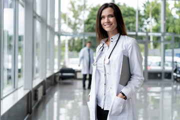 Wall Mural - Portrait of young woman doctor with white coat standing in hospital.