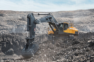 Yellow big excavator in the coal mine, loads the breed, with the bright sun and nice blue sky in the background. Mining truck mining machinery. Technique in coal mine