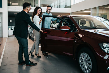 Middle age couple choosing and buying car at car showroom. Car salesman helps them to make right decision.