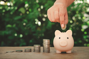 a man hand putting a coin into the piggy bank on a wooden table