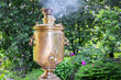 A traditional Russian samovar is heated by wood in the garden. A yellow retro samovar boils water and releases smoke.