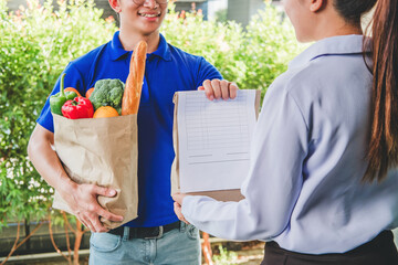 Wall Mural - Food Delivery concept. Asian woman hand accepting bag of food, fruit, vegetable delivery from professional deliveryman Postman and express grocery delivery.