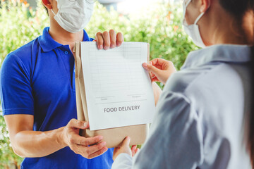 Wall Mural - Asian delivery man wearing face mask hand giving bag of food delivery to female customer grocery delivery service during covid19.