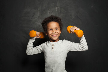 Happy strong black child boy with dumbbells