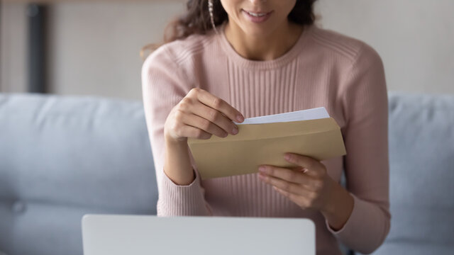 Crop close up of young Caucasian woman hold paper envelope open read postal mail letter at home, female receive post paperwork or document, consider notice or notification correspondence news