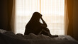 © Kenstocker - silhouette of alone woman sitting on the bed beside the windows with sunlight in the morning