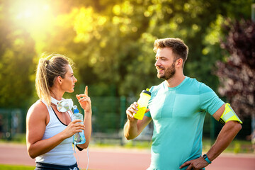 Wall Mural - Happy couple communicating after training on water break in park. Focus on man