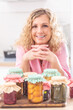 © weyo - Female smiling at camera, leaning above jars of homemade pickles and preserves