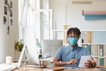 Wall Mural - front view portrait of young african-american photographer wearing mask while reviewing pictures sit