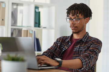 Wall Mural - portrait of contemporary african-american man using laptop and typing while working at desk in offic