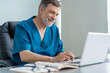 © opolja - Mature male doctor working on laptop computer, sitting in medical office.