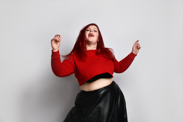 Wall Mural - Obese ginger lady in red spiked top, black bra and leather skirt. She is dancing, posing isolated on white photo background