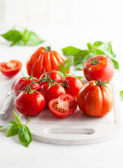 Wall Mural - Assorted fresh ripe tomatoes and basil on white board. Healthy food concept. Clean eating