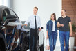 © Юрий Дровнин - Selective focus Manager of a car dealership showing a luxury car to spouses in a car dealership. The concept of professionalism, the lease agreement, car rental, retail sales
