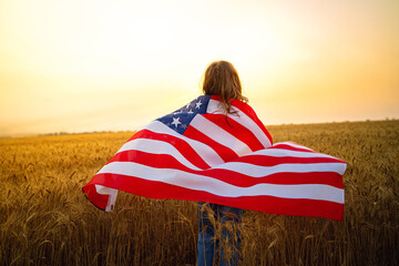 Adorable patriotic girl wearing an American flag in a beautiful wheat field.