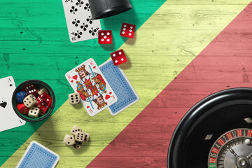 Wall Mural - Republic Of The Congo casino theme. Aces in poker game, cards and chips on red table with national wooden flag background. Gambling and betting.