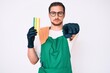 © Krakenimages.com - Young handsome man wearing apron holding scourer pointing with finger to the camera and to you, confident gesture looking serious