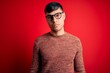 © Krakenimages.com - Young handsome hispanic man wearing nerd glasses over red background Relaxed with serious expression on face. Simple and natural looking at the camera.