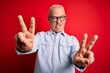 © Krakenimages.com - Middle age handsome hoary man wearing casual striped shirt and glasses over red background smiling with tongue out showing fingers of both hands doing victory sign. Number two.