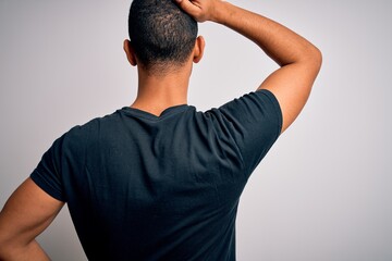 Young handsome african american man wearing casual t-shirt standing over white background Backwards thinking about doubt with hand on head