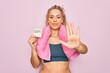 © Krakenimages.com - Beautiful blonde sporty woman doing sport wearing towel holding reminder with diet message with open hand doing stop sign with serious and confident expression, defense gesture