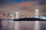 Fototapeta  - Tokyo Destinations. View of Rainbow Bridge in Odaiba Island in Tokyo At Twilight with Line of Skyscrapers in Background.