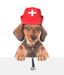 Dachshund puppy dressed like a doctor with medical hat and stethoscope looks above white banner. isolated on white background. Empty space for text