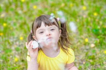 Little girl with syndrome down blows bubbles in a summer park