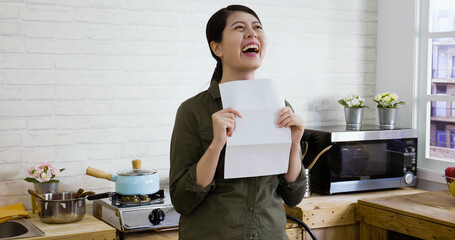 Excited girl reading letter knowing good news while standing in kitchen island at home. happy young female look through paperwork receive positive feedback. woman student with positive exam result