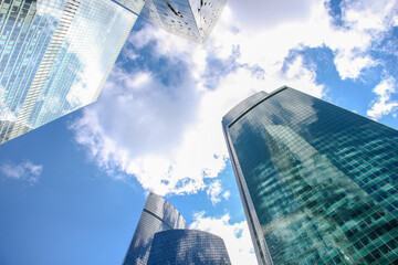 Low angle view of large skyscrapers covered with glass. Blue sky with some white clouds in the background. Modern office buildings theme.