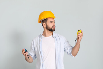 Young man with measuring tapes on light background