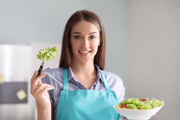 Beautiful young woman eating vegetable salad in kitchen