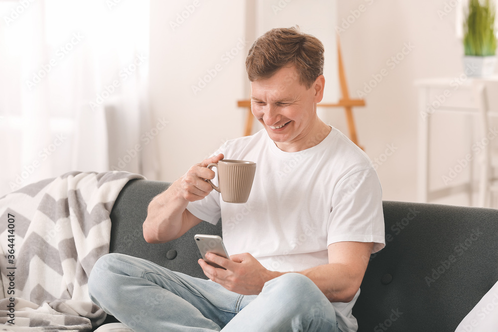 Handsome man with mobile phone drinking tea at home